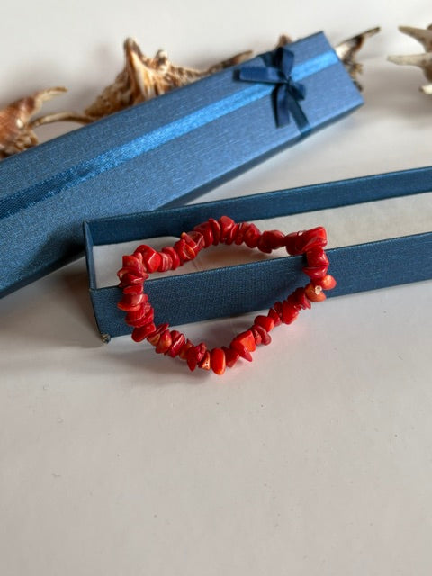 Zierliches rotes Korallen-Stretcharmband vor einer blauen Schmuckschachtel