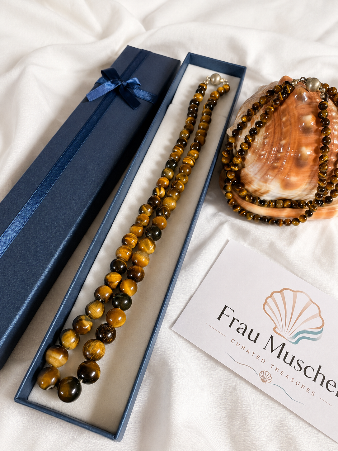 Vintage Tigerauge Halskette aus echtem Tigerauge in einer blauen Schmuckschatulle. Natursteinschmuck mit 925 Silberverschluss und dekorativer Muschel auf weißem Stoff.