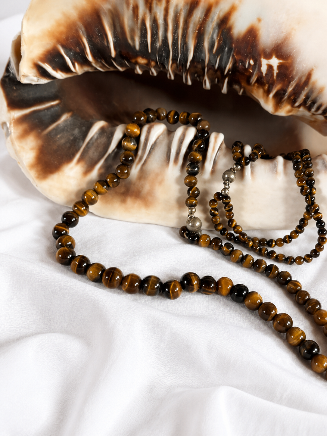 Vintage Tigerauge Schmuckset aus echtem Tigerauge mit Halskette, Armband und 925 Silberverschluss auf einer dekorativen Muschel. Eleganter Natursteinschmuck in goldbraunen Farbtönen.