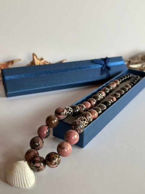 Handgefertigte Rhodonit-Kette mit verzierten Metallperlen neben Schmuckschachtel