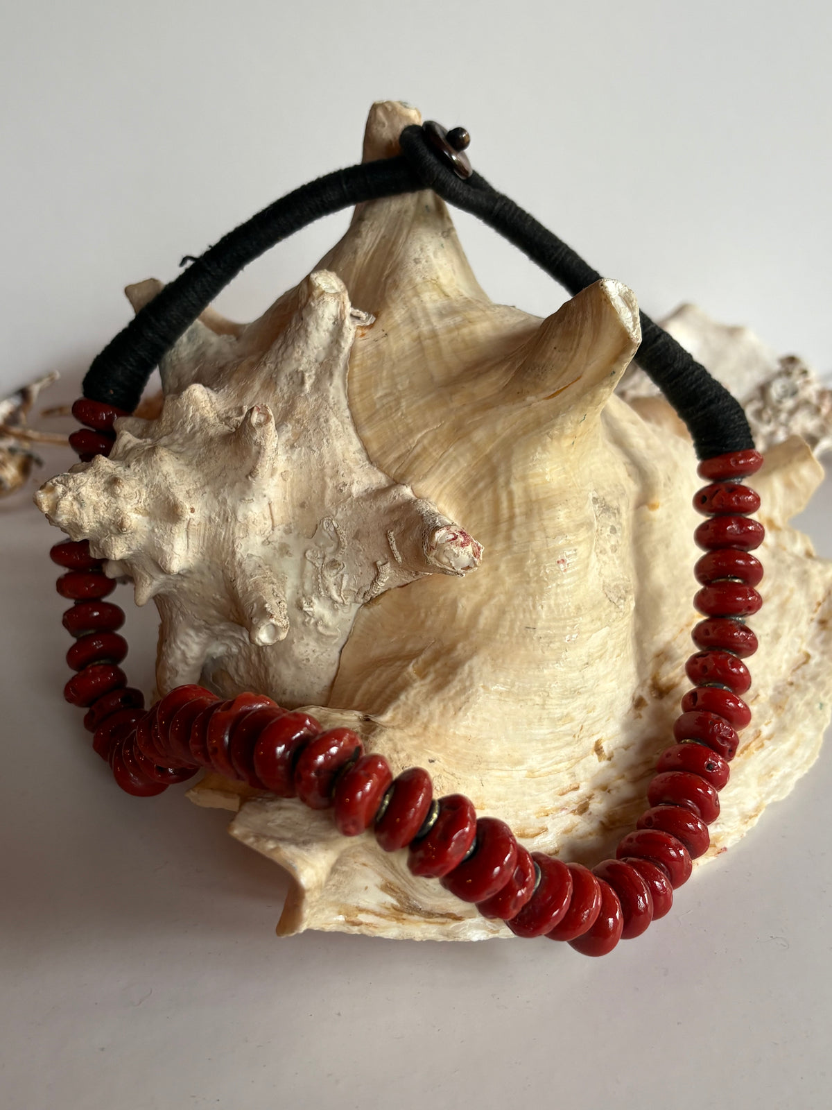 Vintage Korallenkette mit schwarzen, fadenumwickelten Textilsträngen auf einer Muschel