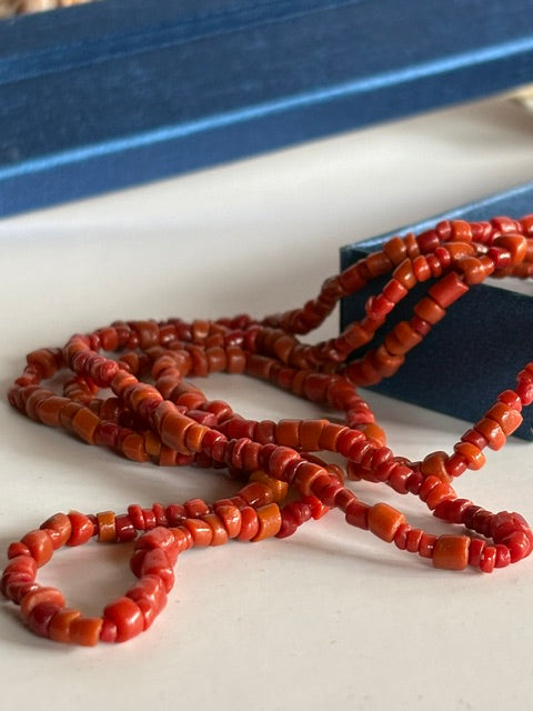 Nahaufnahme der kleinen rot-orangefarbenen Perlen der Vintage-Korallenkette S199 in einer blauen Schmuckschachtel