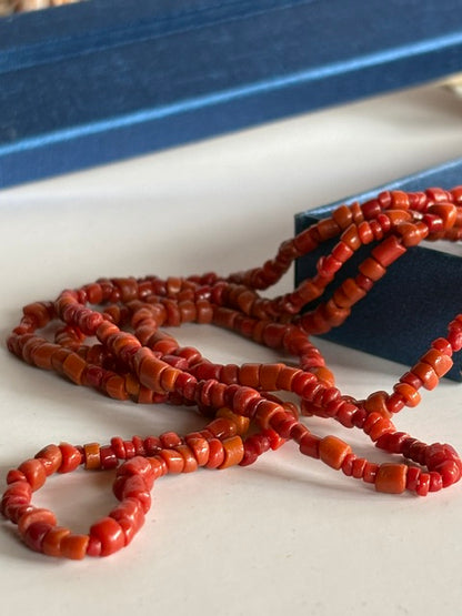 Nahaufnahme der kleinen rot-orangefarbenen Perlen der Vintage-Korallenkette S199 in einer blauen Schmuckschachtel