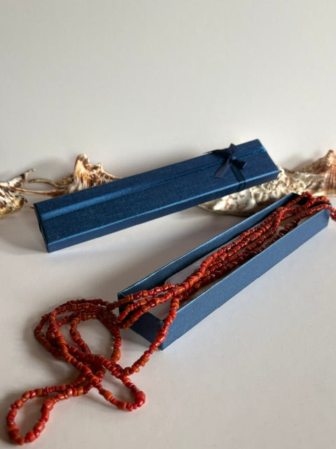 Lange Vintage-Korallenkette in warmen Rottönen neben einer geöffneten blauen Schmuckschachtel mit maritimer Dekoration