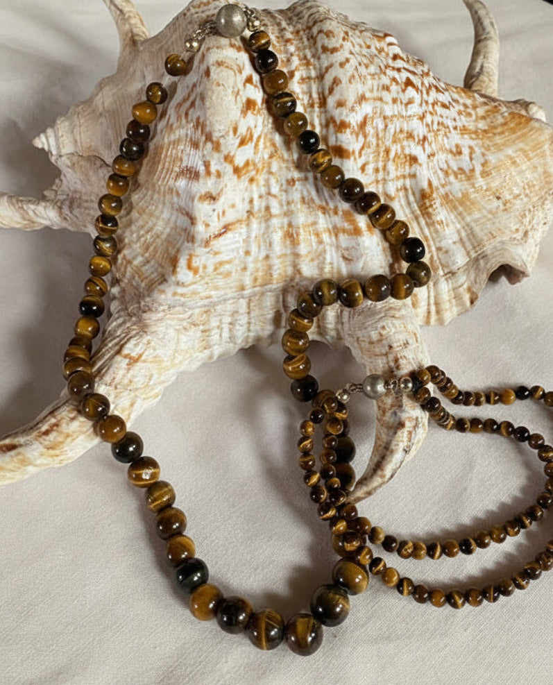 Vintage Tigerauge Schmuckset aus echter Tigerauge-Halskette und passendem Armband auf dekorativer Muschel präsentiert. Natursteinschmuck mit 925 Silberverschluss in warmen Gold- und Brauntönen.