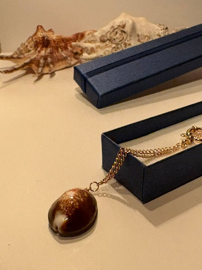 Natural brown cowrie shell pendant with distinctive cream markings on a delicate gold-tone chain.