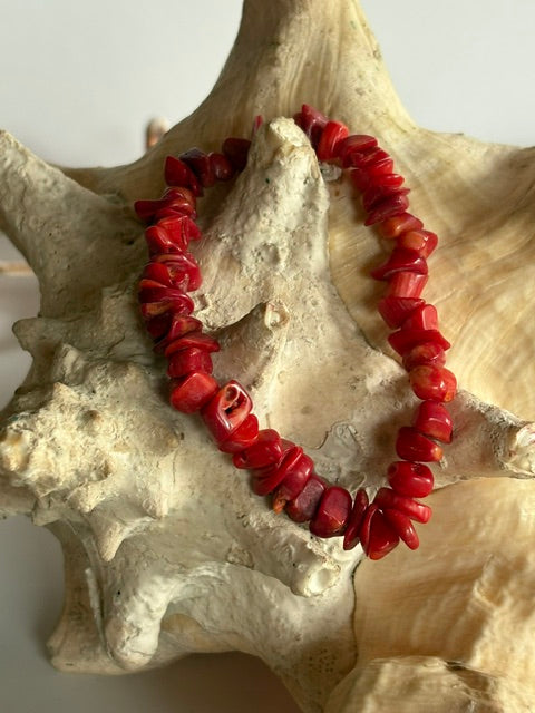 Rotes elastisches Korallenarmband für schmale Handgelenke auf einer Muschel