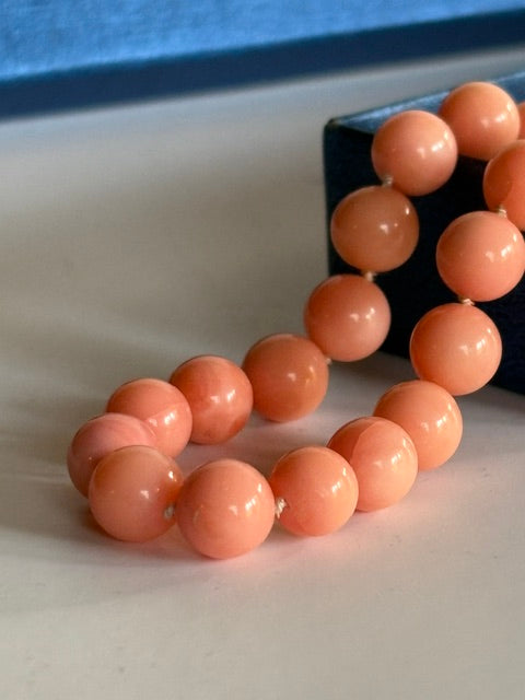 Nahaufnahme lachsfarbener Korallenperlen mit helleren Zeichnungen und Knoten zwischen den Perlen