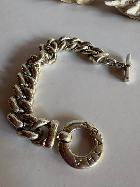 Close-up of the AGATHA lettering on the circular toggle clasp of a silver-tone chain bracelet.