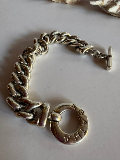 Close-up of the AGATHA lettering on the circular toggle clasp of a silver-tone chain bracelet.