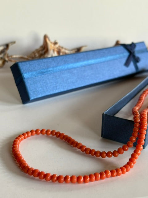 Detail der kleinen rotorangefarbenen Korallenperlen vor einer blauen Schmuckschachtel
