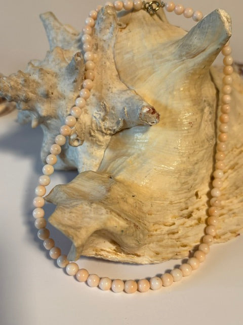 Vintage-Korallenkette mit rundlichen Perlen in Cremeweiß und zartem Rosé auf großer Muschel dekoriert