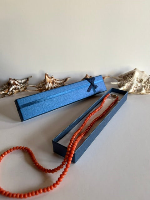 Lange Vintage-Korallenkette über einer offenen blauen Schmuckschachtel mit Muscheln im Hintergrund