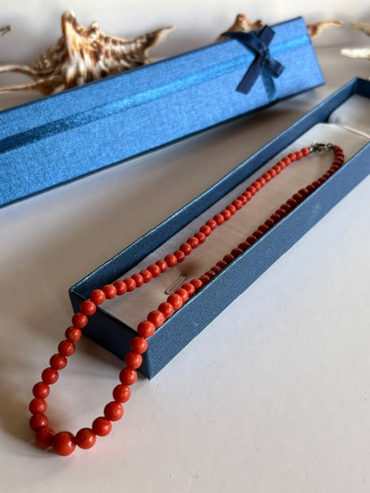 Vintage-Korallenkette mit Perlen im Größenverlauf über einer offenen blauen Schmuckschachtel