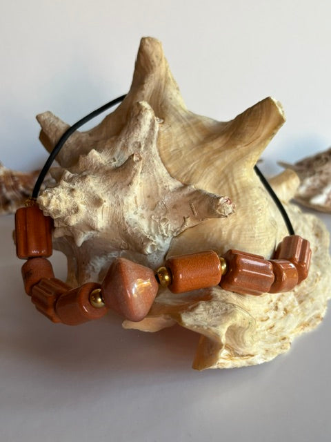 Kupferoranges Keramikcollier mit schwarzem Band dekorativ auf einer Muschel